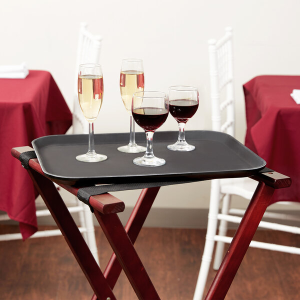 A Carlisle black non-skid fiberglass serving tray with wine glasses and a glass of red wine on it.