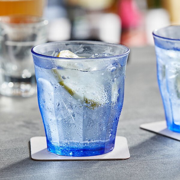 A Duralex Picardie blue glass with ice and a lemon on a table.