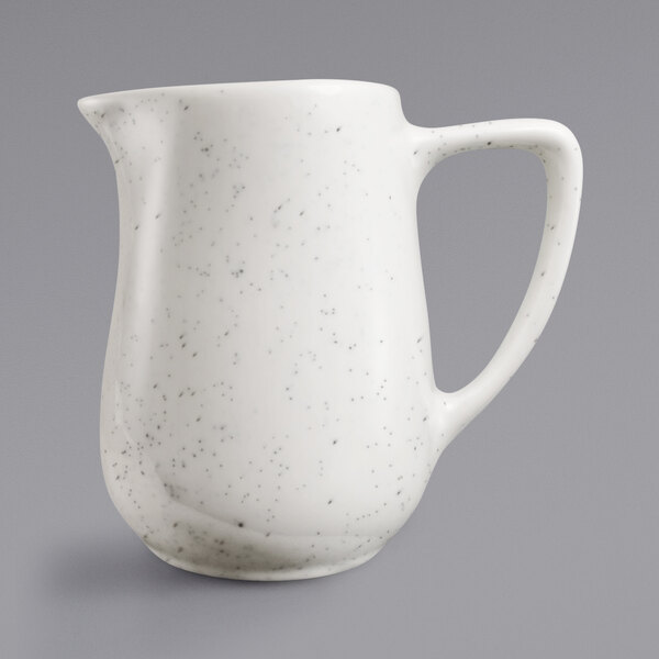 An ivory stoneware creamer with a speckled brown design and a handle.