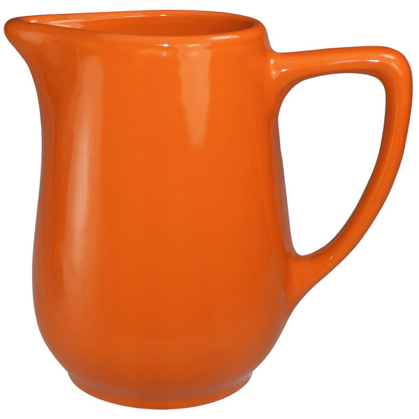A close-up of an orange stoneware creamer with a handle.