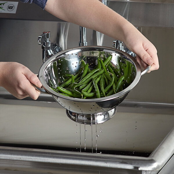 A person using a Vollrath stainless steel colander to wash green beans.