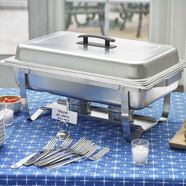 A Sterno 8 quart stainless steel chafer set on a table with silverware and candles.