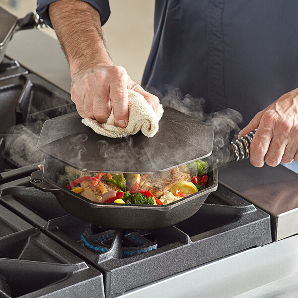 A person cooking food in a FINEX cast iron skillet on a stove.