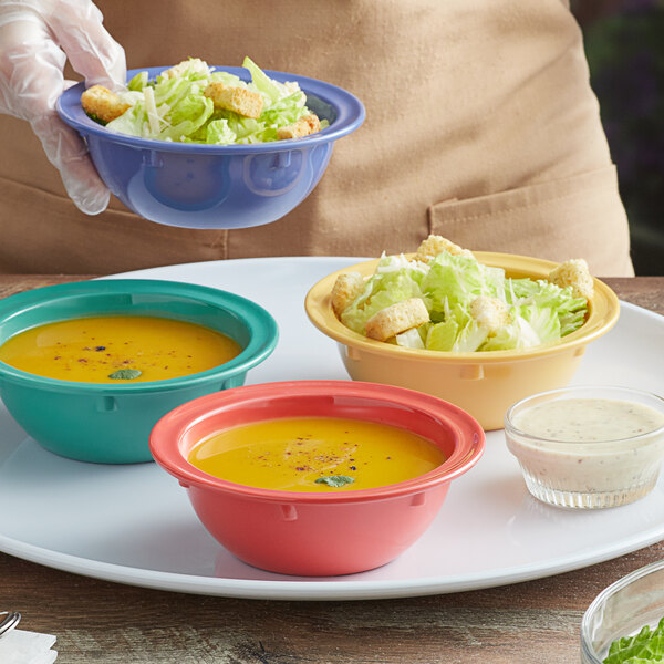 A person holding a bowl of salad with a clear bowl of soup on a table with three bowls of food.