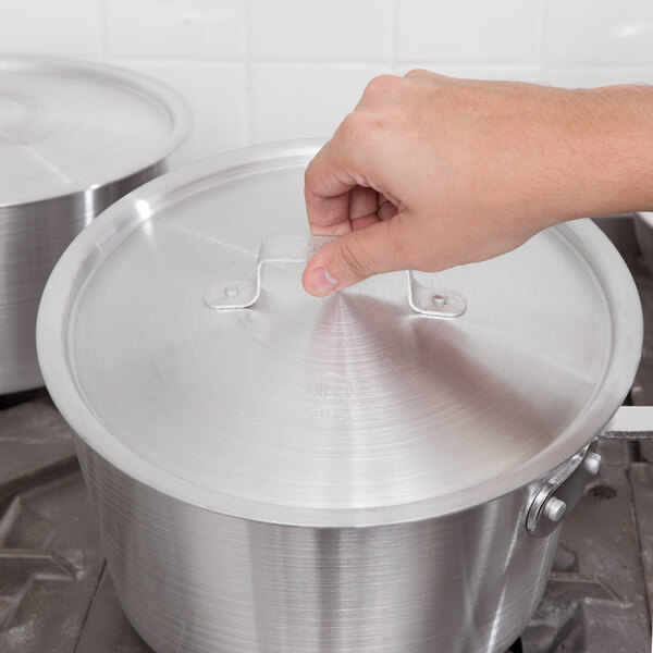 A hand placing a white Vollrath Arkadia lid on a metal pot on a stove.