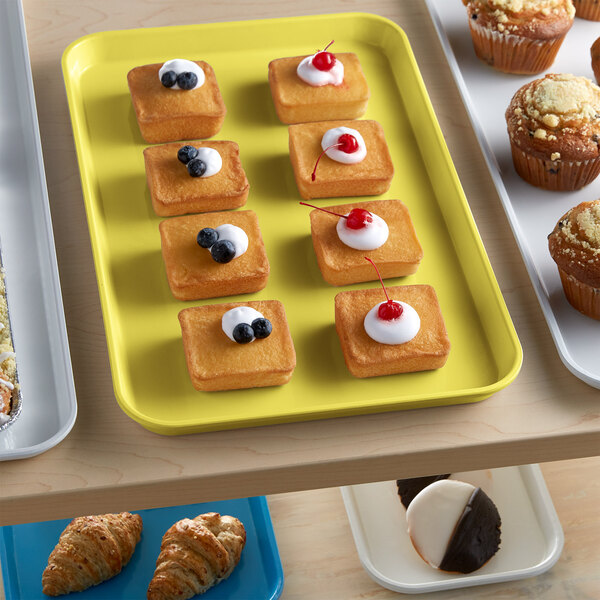 A yellow Cambro market tray with pastries and muffins on a table.