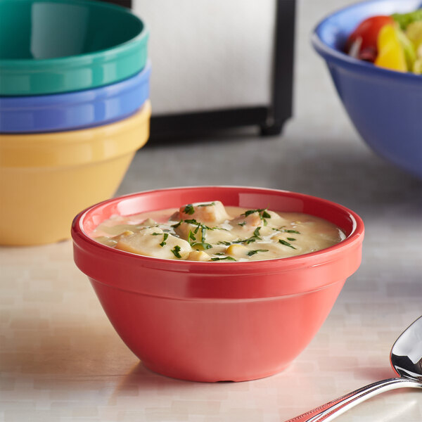 An Elite Global Solutions Brazil assorted color melamine bouillon cup filled with soup on a stack of colorful bowls.