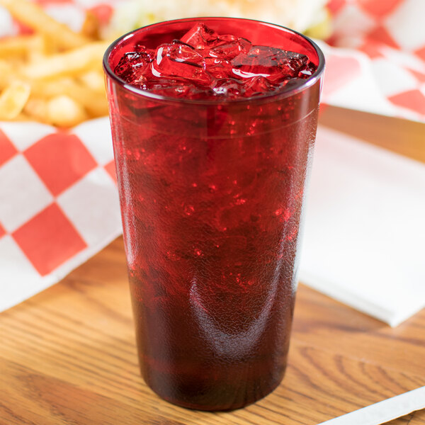 A stack of Carlisle ruby plastic tumblers filled with red drinks and ice on a table with fries.