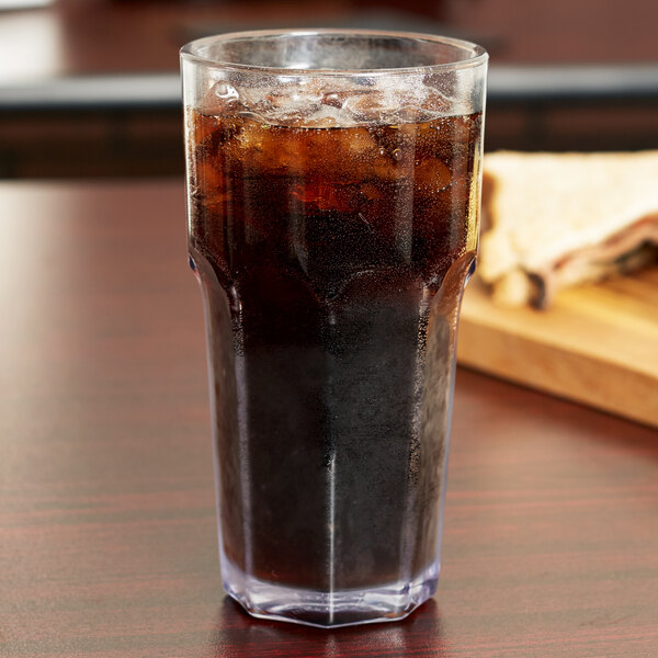 A Carlisle clear plastic tumbler filled with soda on a table.
