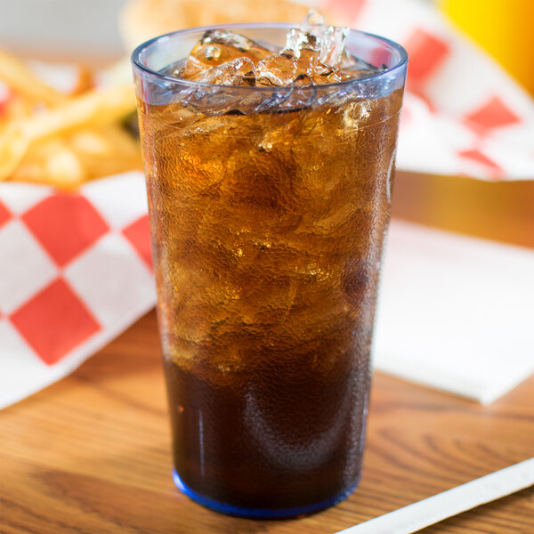 A Carlisle blue plastic tumbler filled with a brown liquid and ice on a table with fries and a straw.