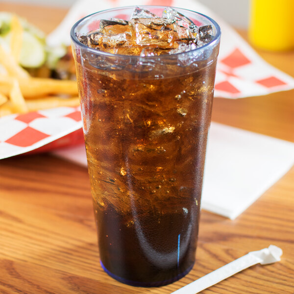 A blue Carlisle plastic tumbler filled with soda and ice on a table with fries