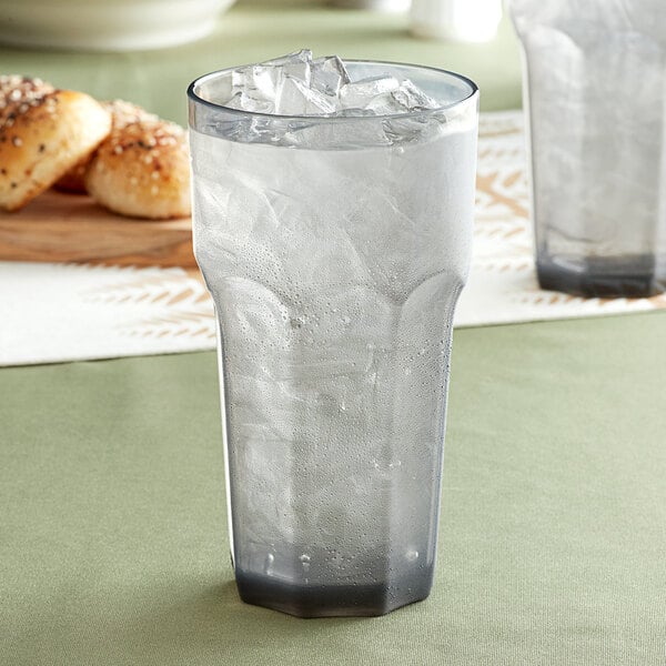 A Carlisle Louis smoke plastic tumbler filled with ice water on a white background.