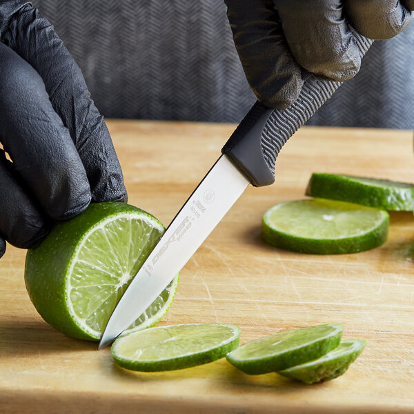 A person in black gloves using a Dexter-Russell SofGrip paring knife to cut a lime.