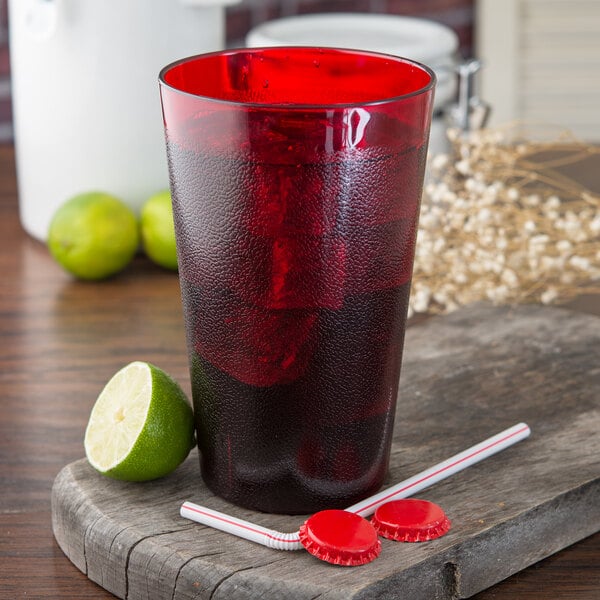 A Carlisle ruby plastic tumbler filled with red liquid, ice, and limes with a straw.