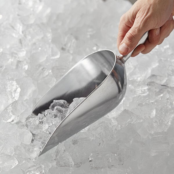 A hand holding a Vollrath cast aluminum ice scoop over ice.