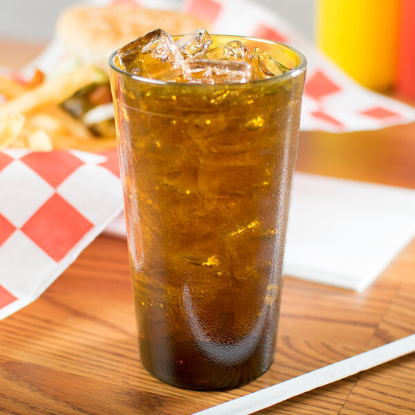 A Carlisle amber plastic tumbler filled with ice tea on a table with a burger and fries.