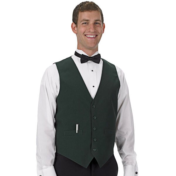A man wearing a Henry Segal hunter green server vest and bow tie smiles in a cocktail bar.