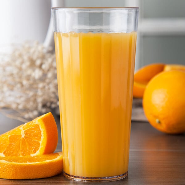 A Carlisle clear plastic tumbler filled with orange juice with a slice of orange on the rim.