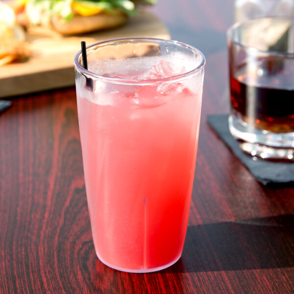 A Carlisle clear polycarbonate tumbler filled with a pink drink, ice, and a straw.