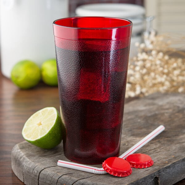 A Carlisle Ruby plastic tumbler filled with red liquid and a lime with a straw.