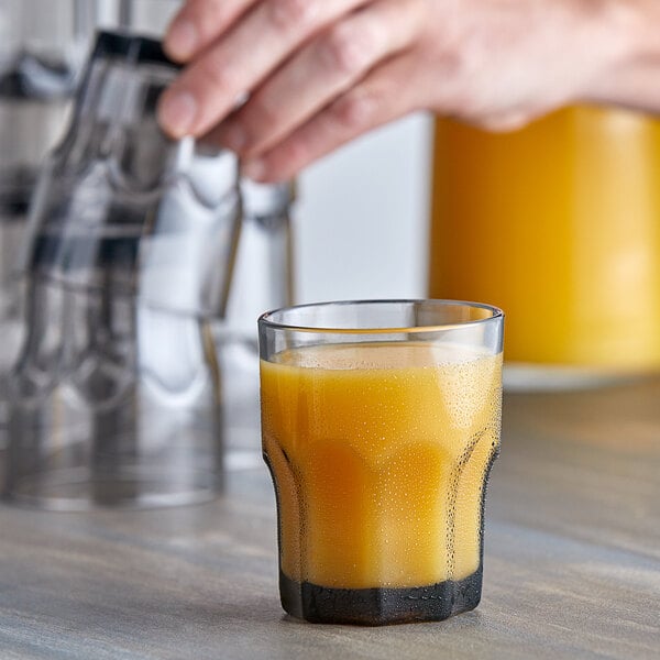 A hand pouring orange juice into a Carlisle SAN plastic tumbler on a counter.
