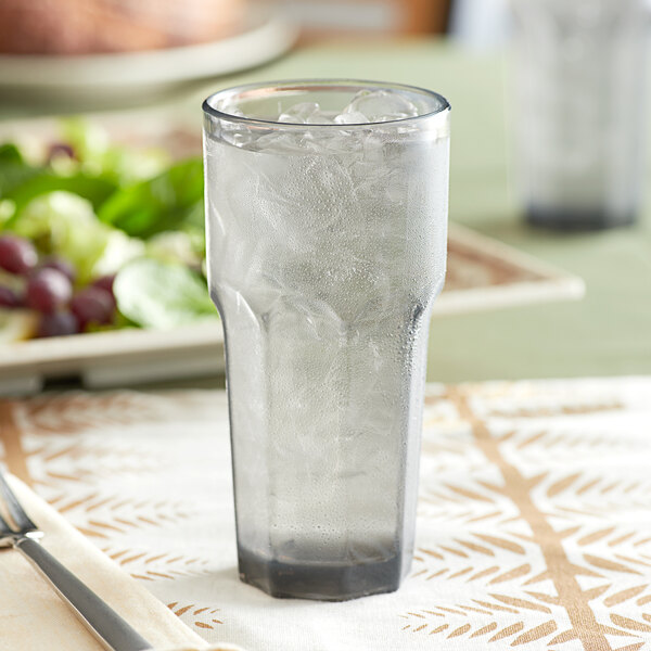 A Carlisle Louis smoke plastic tumbler filled with ice water on a table.