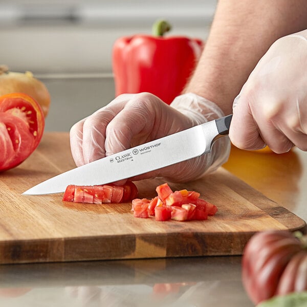 A person uses a Wusthof forged utility knife to cut tomatoes on a cutting board.