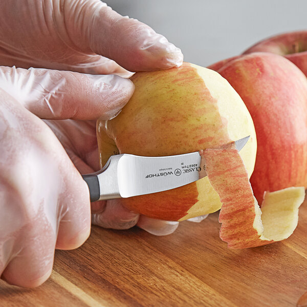 A person peeling a red apple with a Wusthof Classic forged peeling knife.