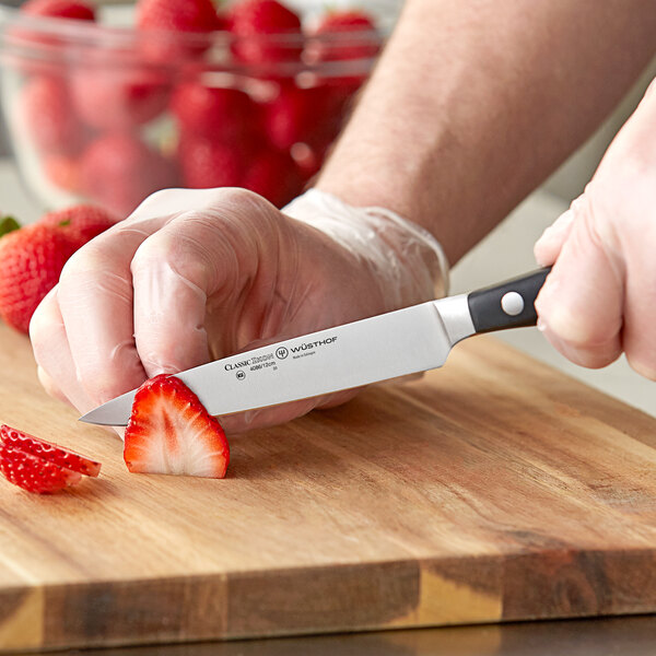 A person using a Wusthof Classic Ikon forged utility knife to cut a strawberry on a cutting board.