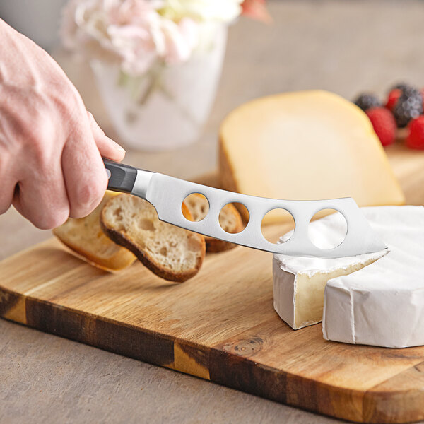 A person using a Wusthof Classic forged soft cheese knife to cut cheese on a cutting board.