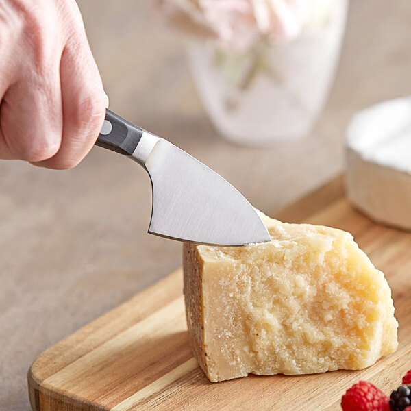 A hand uses a Wusthof Classic Parmesan Cheese Knife to cut a piece of cheese.