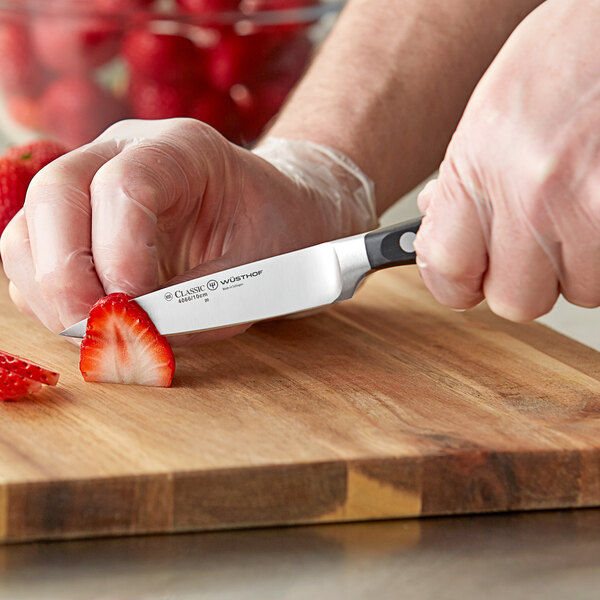 A person cutting strawberries with a Wusthof Classic forged paring knife on a cutting board.