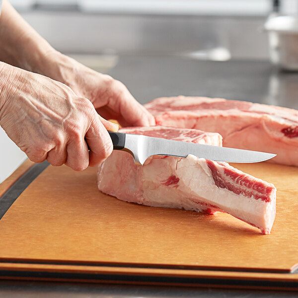 A person using a Wusthof Classic boning knife to cut meat on a cutting board.