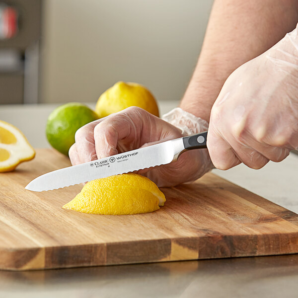 A person using a Wusthof Classic serrated utility knife to cut a lemon on a cutting board.