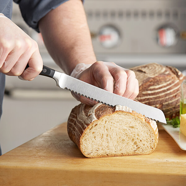A person cutting a loaf of bread with a Wusthof serrated bread knife.