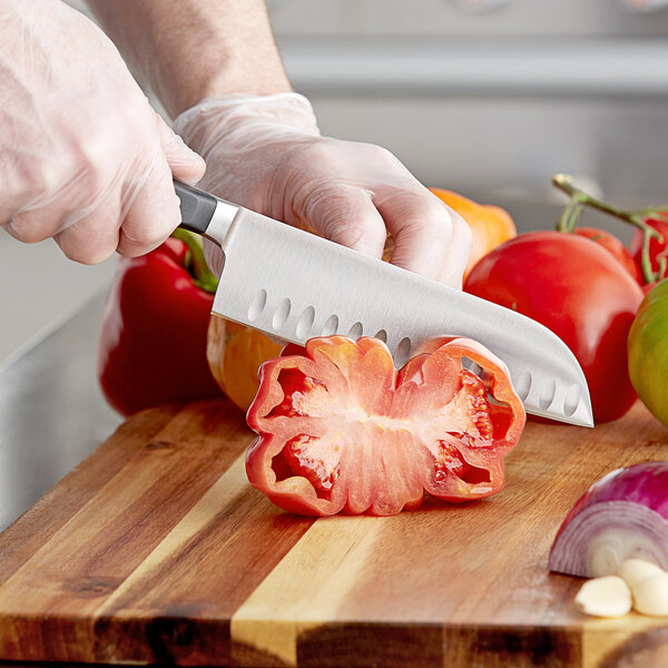 A person using a Wusthof Classic Santoku knife to cut a tomato.