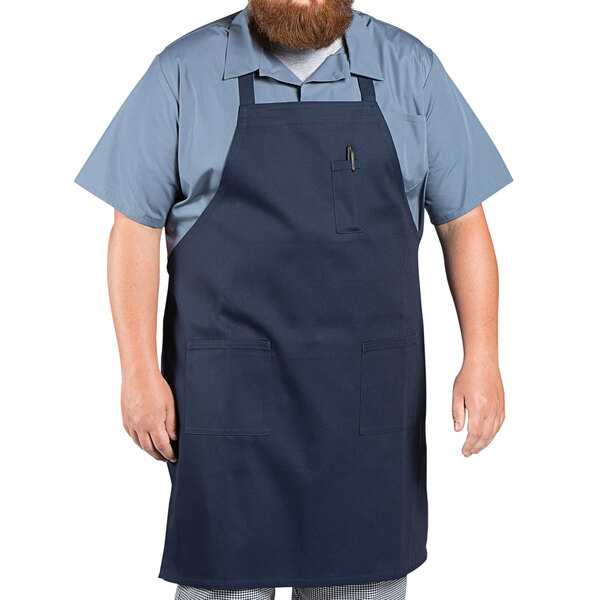 A man with a beard wearing a navy blue Uncommon Chef bib apron with three pockets.