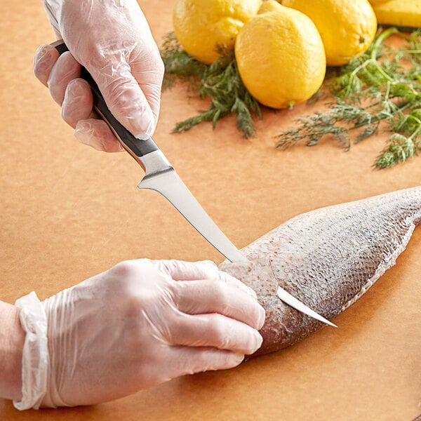 A person using a Wusthof Classic Ikon fillet knife to cut a fish on a table.