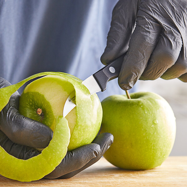 A hand peeling a green apple with a Wusthof peeling knife.
