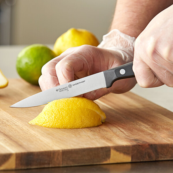 A person using a Wusthof utility knife to cut a lemon on a cutting board.
