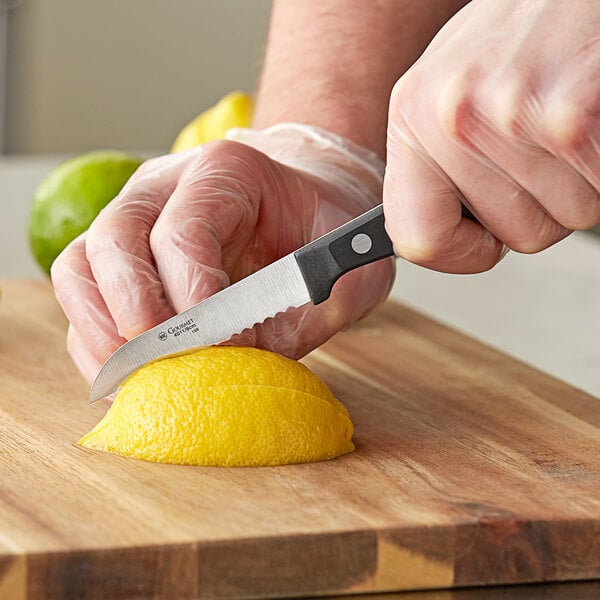 A person's hand using a Wusthof serrated paring knife to cut a lemon.