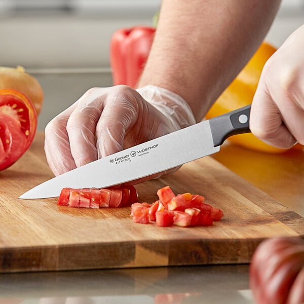 A person using a Wusthof Gourmet utility knife to cut a tomato.