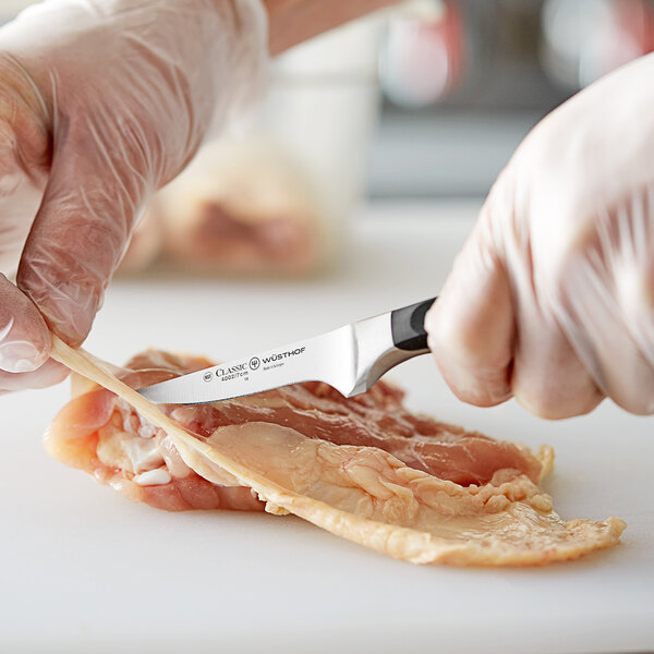 A person in gloves using a Wusthof Classic trimming knife to cut up meat on a counter.