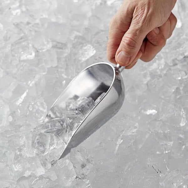 A hand using a Vollrath cast aluminum ice scoop to scoop ice.