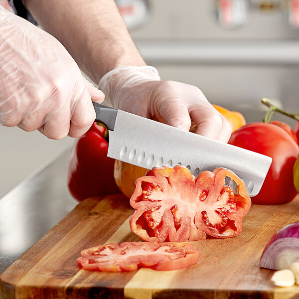 A person in gloves uses a Wusthof Nakiri knife to cut tomatoes on a cutting board.