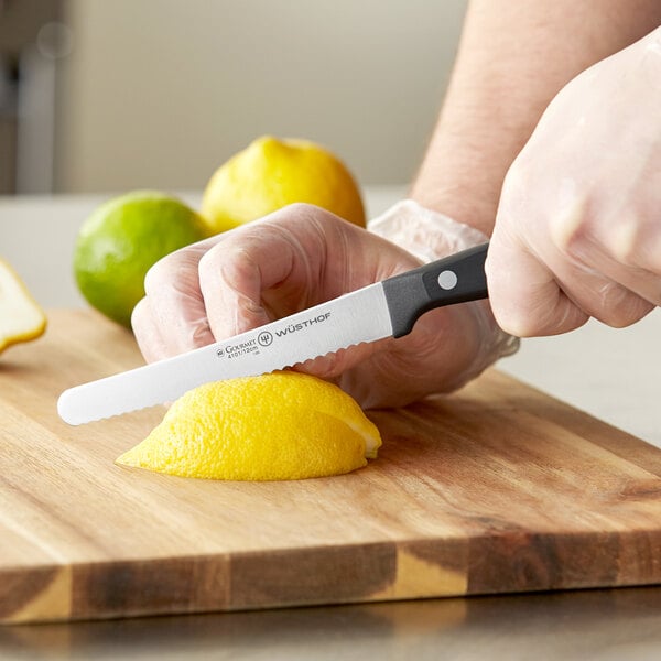 A person using a Wusthof Gourmet serrated utility knife to cut a lemon on a cutting board.