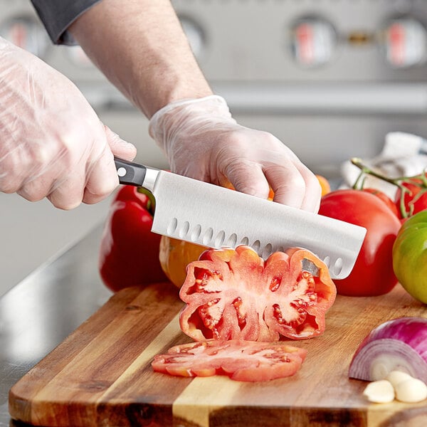 A person in gloves using a Wusthof Classic Nakiri knife to cut tomatoes on a cutting board.