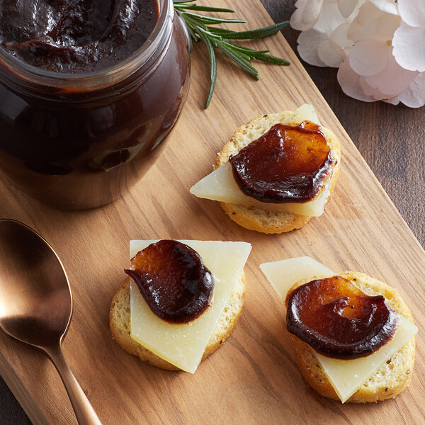 A piece of bread with cheese and Dalmatia Plum Spread on top on a board with other food.