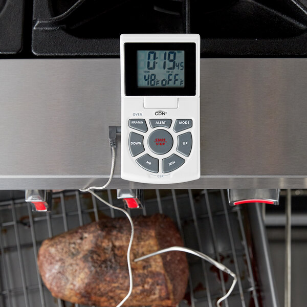 A white CDN digital thermometer with a cord checking the temperature of meat on a grill.