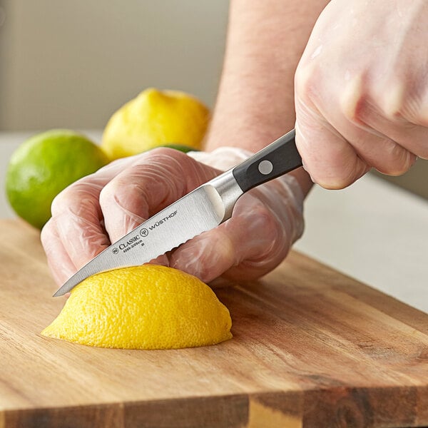 A person using a Wusthof Classic serrated paring knife to cut a lemon.